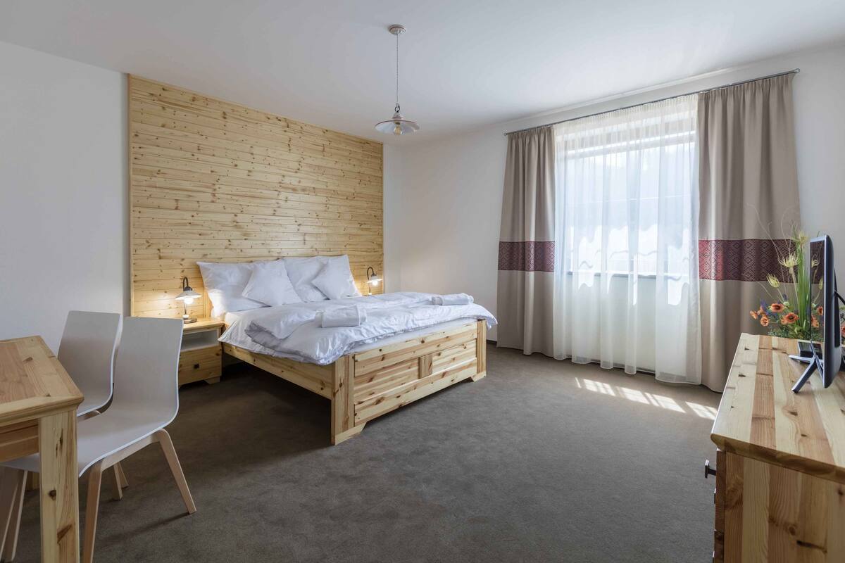 Un dormitorio con cabecera de madera, cama con ropa de cama blanca, escritorio con silla y mesita de noche con lámpara.