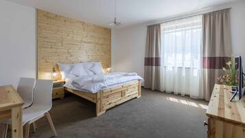 A bedroom with a wooden headboard, a bed with white bedding, a desk with a chair, and a bedside table with a lamp.