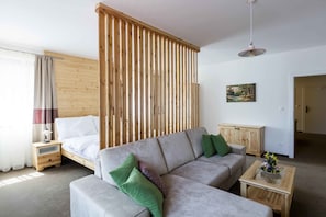 Uma sala de estar moderna com sofá, cama, divisória de madeira, uma mesa pequena com flores e um quadro na parede.