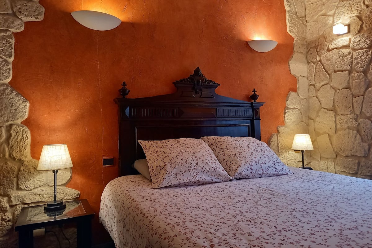 A bedroom with a stone wall, a wooden headboard, two bedside lamps, and a floral bedspread.