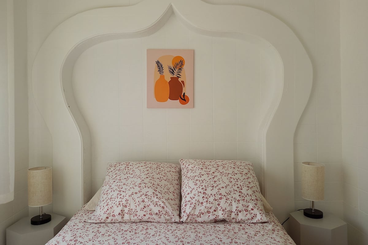 A bed with floral bedding, a wall-mounted artwork of vases, and bedside lamps on nightstands.