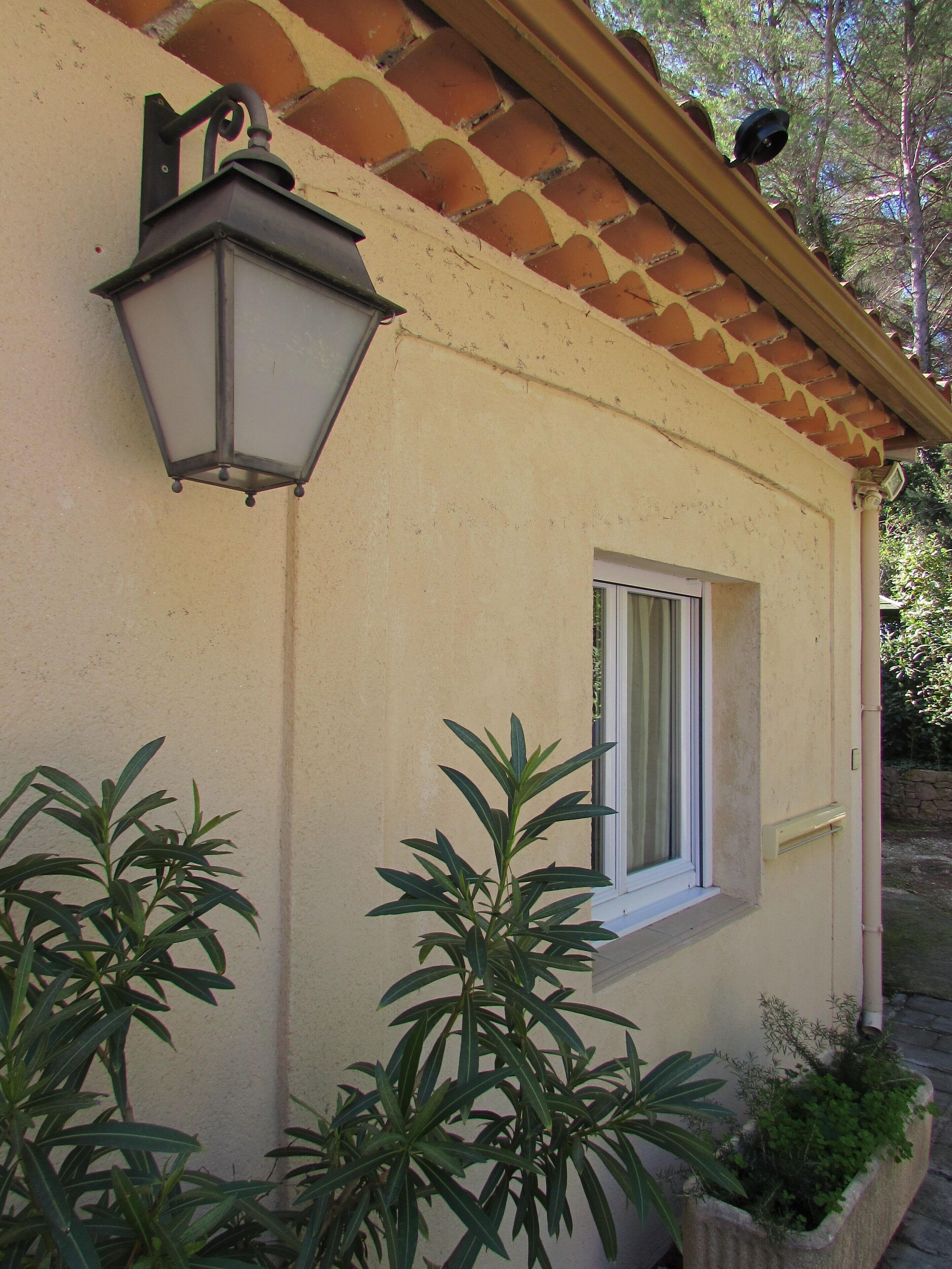 A building with a tiled roof, a window with white shutters, and a wall-mounted light fixture.