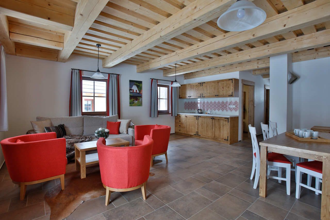 A spacious living area with a wooden ceiling, a dining table with chairs, and a kitchen area with wooden cabinets.