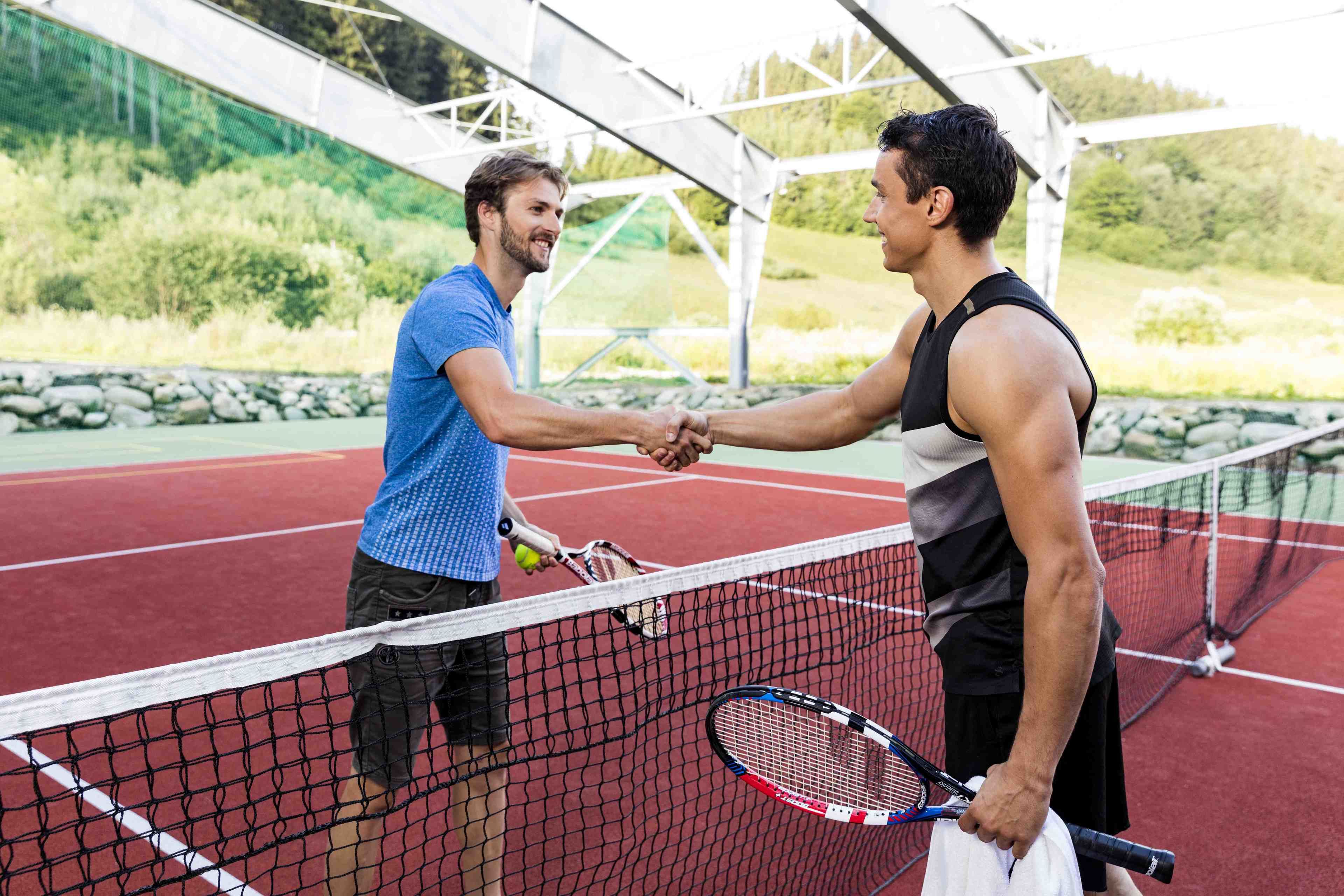 Deux personnes se serrent la main sur un court de tennis, avec un filet au milieu.