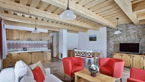 Un salón espacioso con techo de madera, un sofá, sillones rojos, una mesa de centro de madera y una cocina al fondo.