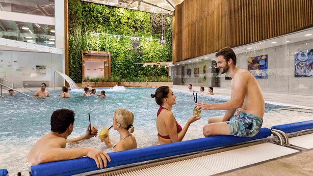 Una piscina interior con gente relajándose e interactuando.