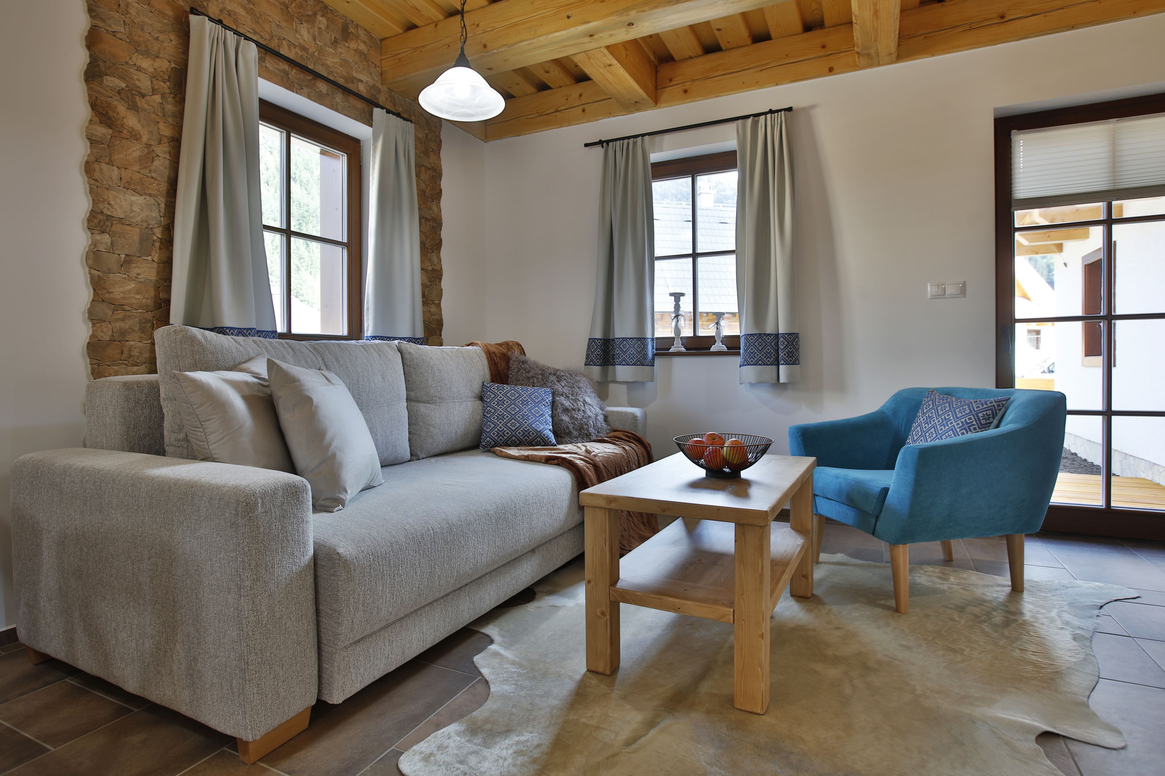 A living room with a grey sofa, a blue armchair, a wooden coffee table, and a stone wall.