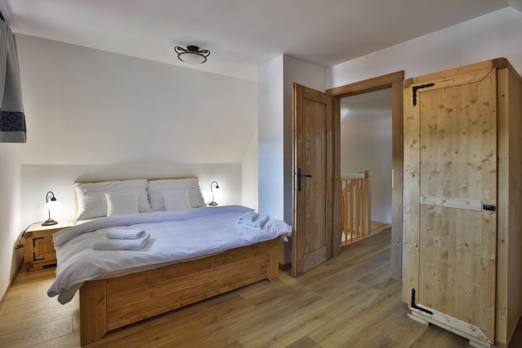 A bedroom with a wooden bed, white bedding, a nightstand with a lamp, and a wooden wardrobe.