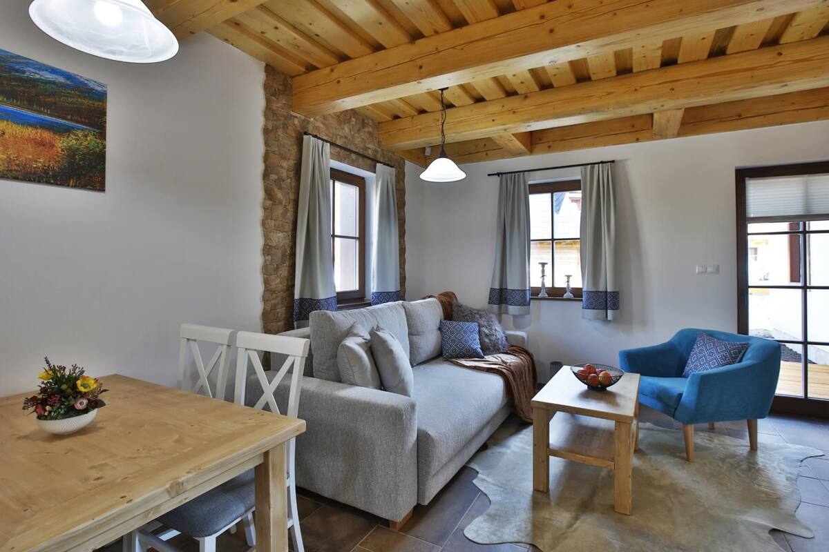 A cozy living room with a sofa, a blue armchair, a wooden table, and a stone wall.
