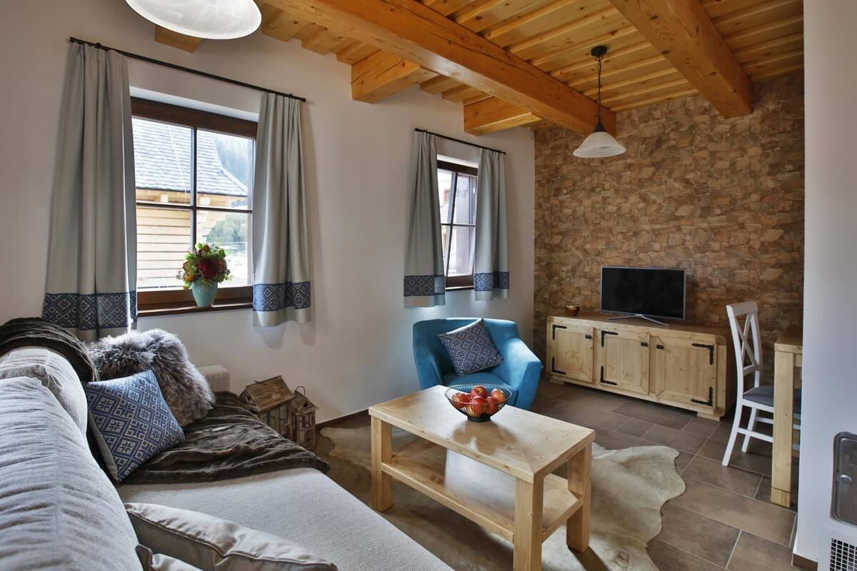 A cozy living room with a sofa, a blue armchair, a wooden coffee table, and a stone wall.