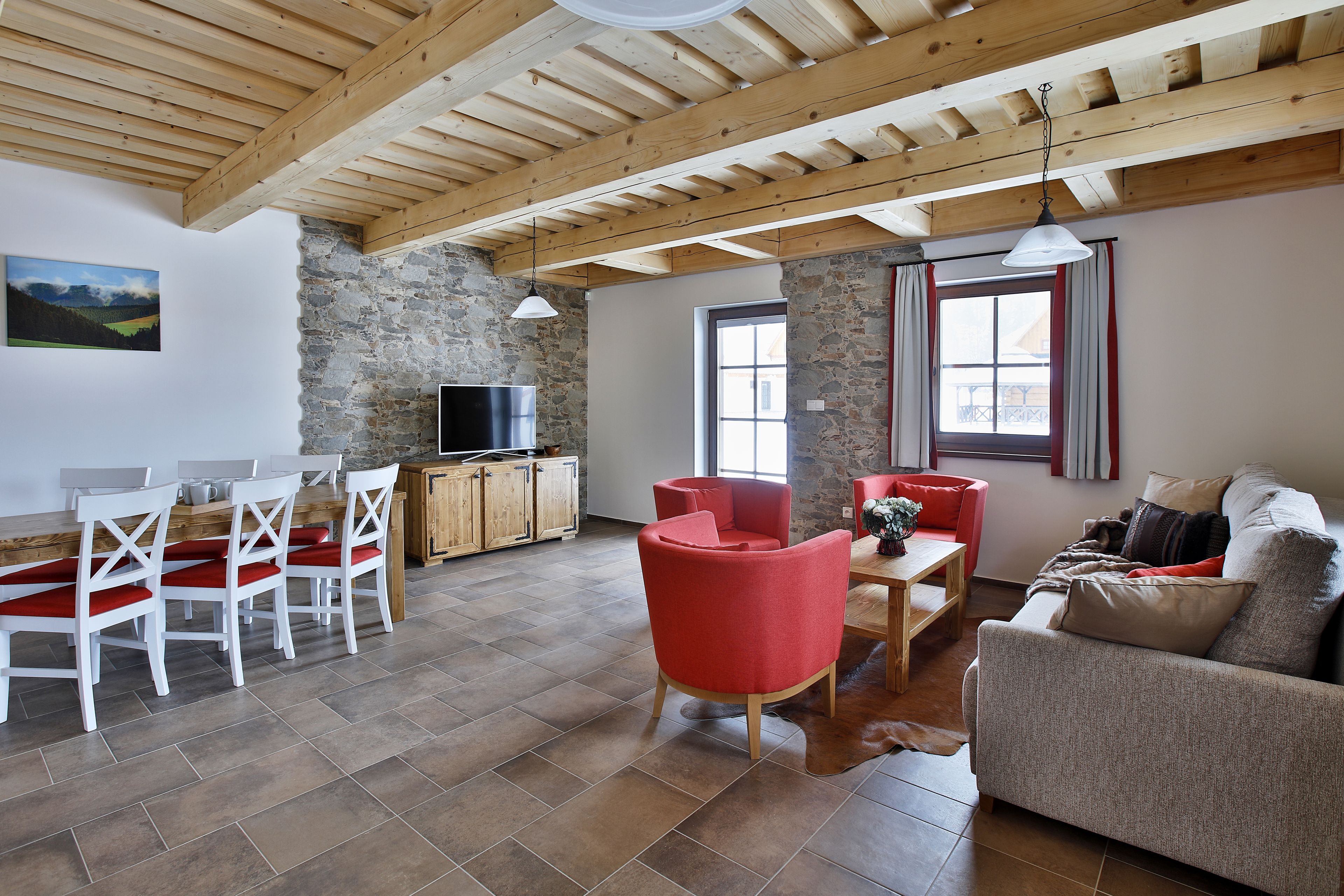 Amplia sala de estar con techo de madera alto, paredes de piedra, mesa de comedor de madera con sillas, sofá y televisor sobre un mueble de madera.