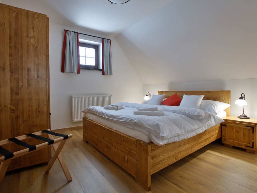 Een slaapkamer met een houten bed, een nachtkastje met een lamp, een raam met gordijnen en een houten garderobekast.