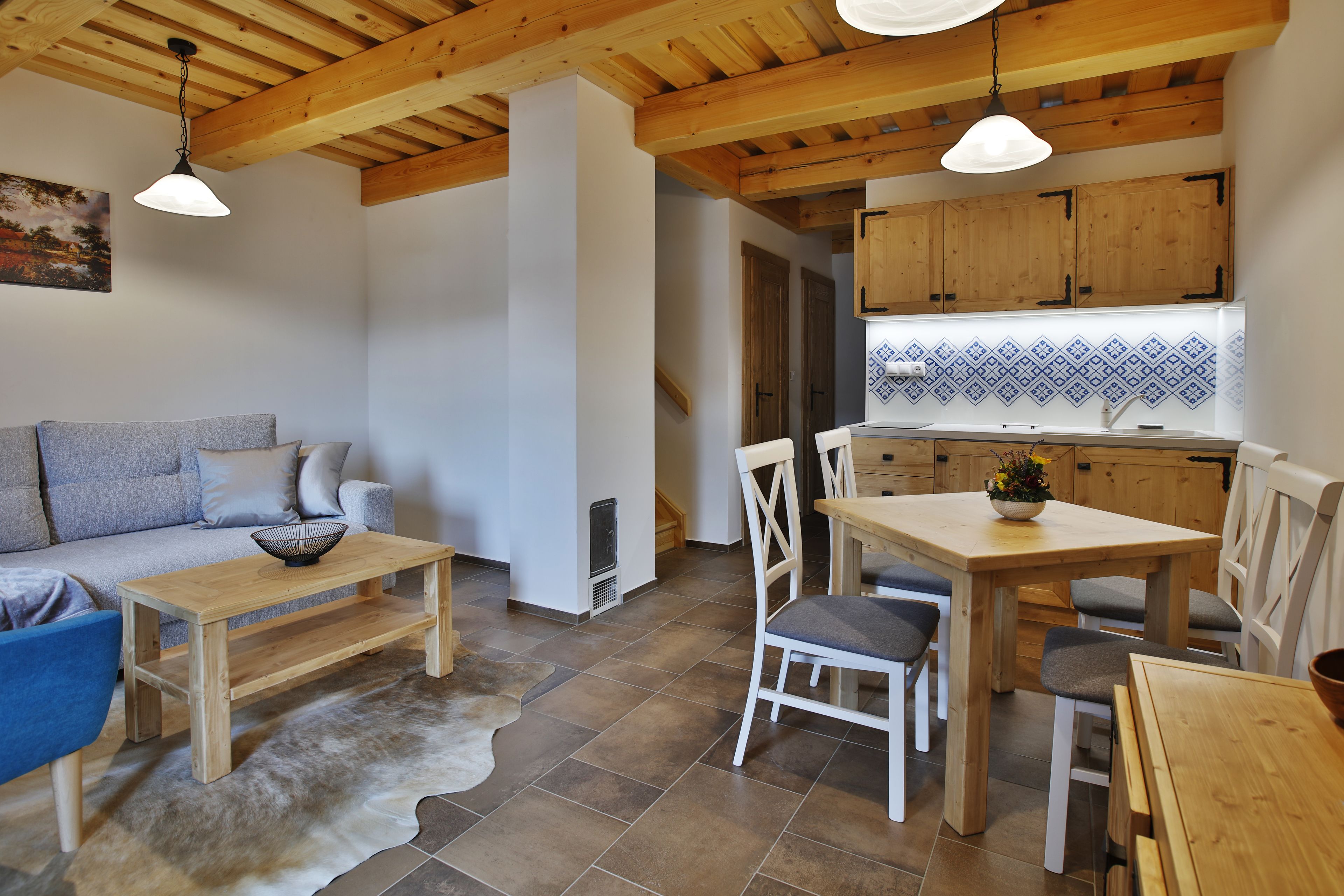 Un salon chaleureux avec une table et des chaises en bois, un canapé et une cuisine dotée de meubles en bois et d’un dosseret carrelé.