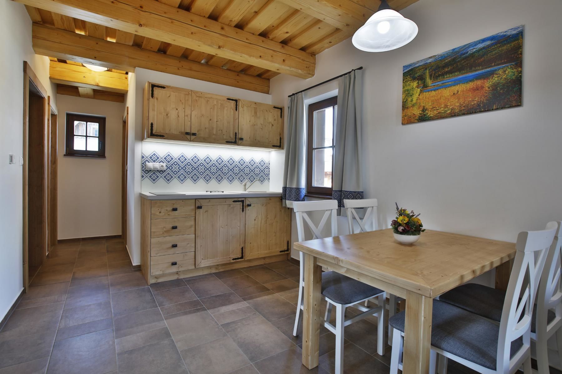 Une cuisine avec des meubles de rangement en bois, une fenêtre avec des rideaux, une table à manger avec des chaises et un tableau accroché au mur.