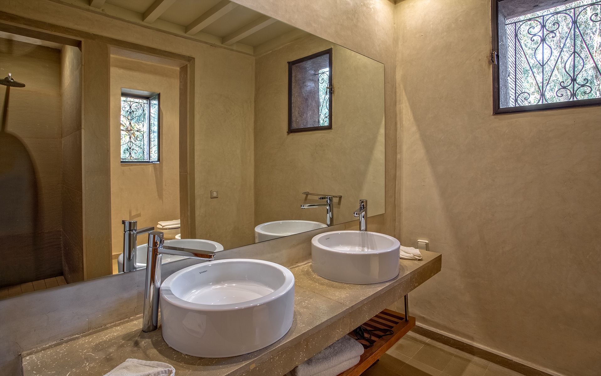 A bathroom with two white sinks, a large mirror, and a window with decorative iron bars.
