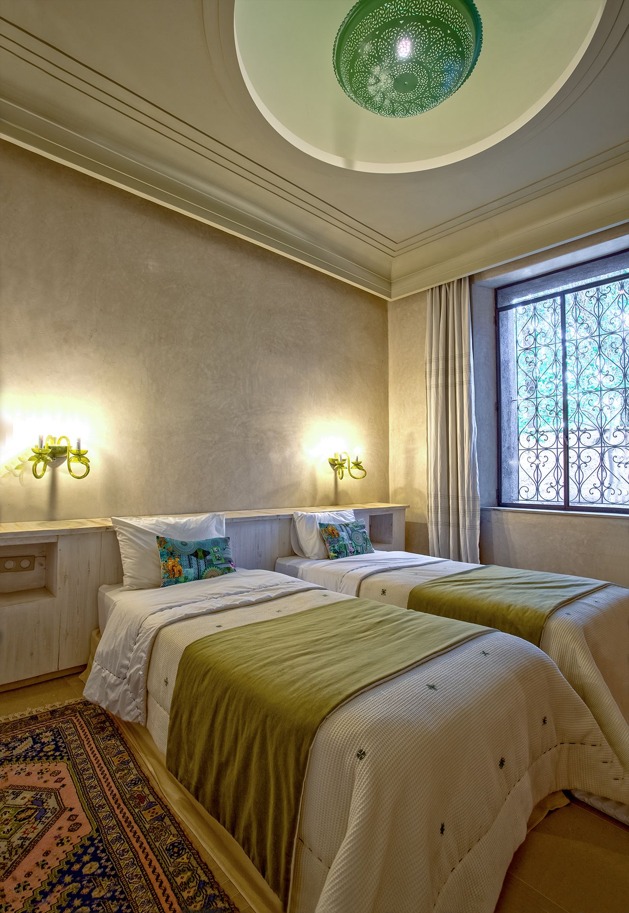 A bedroom with two beds, a patterned rug, and a decorative ceiling light.