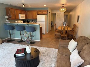 A modern kitchen with wooden cabinets, a central island, bar stools, and a dining area with a wooden table and chairs.