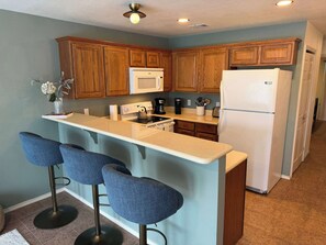 A kitchen with wooden cabinets, a white refrigerator, a microwave, a stove, and bar stools.