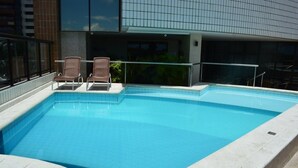 A rectangular swimming pool with two wicker chairs and a glass railing. - OP Flat Vip Frente Mar (Fortaleza)