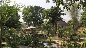 A lush garden with a pond, a wooden deck, and a thatched-roof structure. - Sweet Home Resort at Pai (Pai)