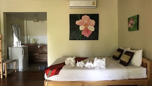 A hotel room with a bed, a wooden headboard, a wall-mounted air conditioner, and a painting of a flower. - Sweet Home Resort at Pai (Pai)