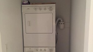 Una lavadora y secadora apiladas, de color blanco y tamaño compacto, en un cuarto de lavado estrecho con piso de madera.