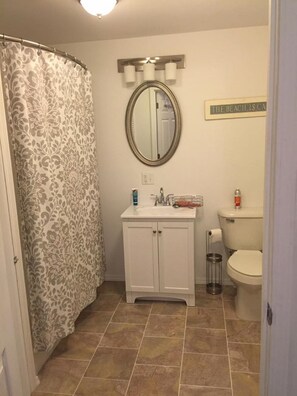 Une salle de bain avec un rideau de douche, un lavabo avec un miroir, des toilettes et un panneau sur le mur.