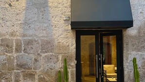 A stone building with a black awning, a numbered door, and two potted cacti. - Hotel Piru Wasi Arequipa (Arequipa)