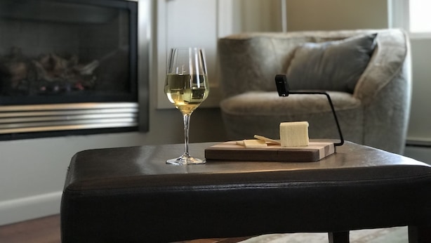 A living room with a fireplace, a glass of white wine, a cutting board with cheese, and a remote control. - High End Apartment in Downtown  Hallowell (Hallowell)