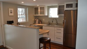 A modern kitchen with white cabinets, a stainless steel refrigerator, a built-in microwave, and a bar stool. - High End Apartment in Downtown  Hallowell (Hallowell)