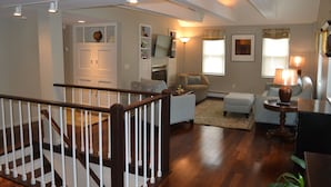 A spacious living room with a wooden staircase, a sofa, a coffee table, and a lamp. - High End Apartment in Downtown  Hallowell (Hallowell)