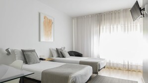 A hotel room with two beds, a desk, a chair, a flat-screen TV, and a large window with sheer curtains. - Hotel Umu (Santarém)