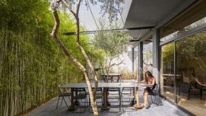 A modern outdoor dining area with a glass wall, a bamboo wall, and a table with chairs. - Hotel Umu (Santarém)