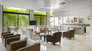 A modern hotel lobby with a bar area, seating arrangements, and large windows offering a view of greenery. - Hotel Umu (Santarém)