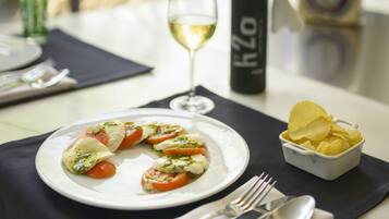 A dining table with a plate of food, a glass of white wine, a bottle of olive oil, and a small bowl of chips.