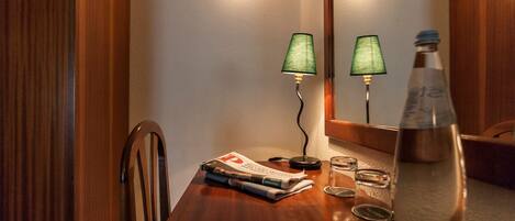 A wooden table with a newspaper, a glass, a bottle, and two lamps.