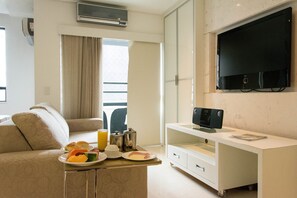 A modern hotel room with a sofa, a dining table with breakfast, a TV, and a large window. - STM Flat Meu Lugar Ceará (Fortaleza)