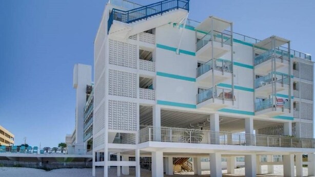 Un hotel de varios pisos con balcones, situado en una playa de arena.