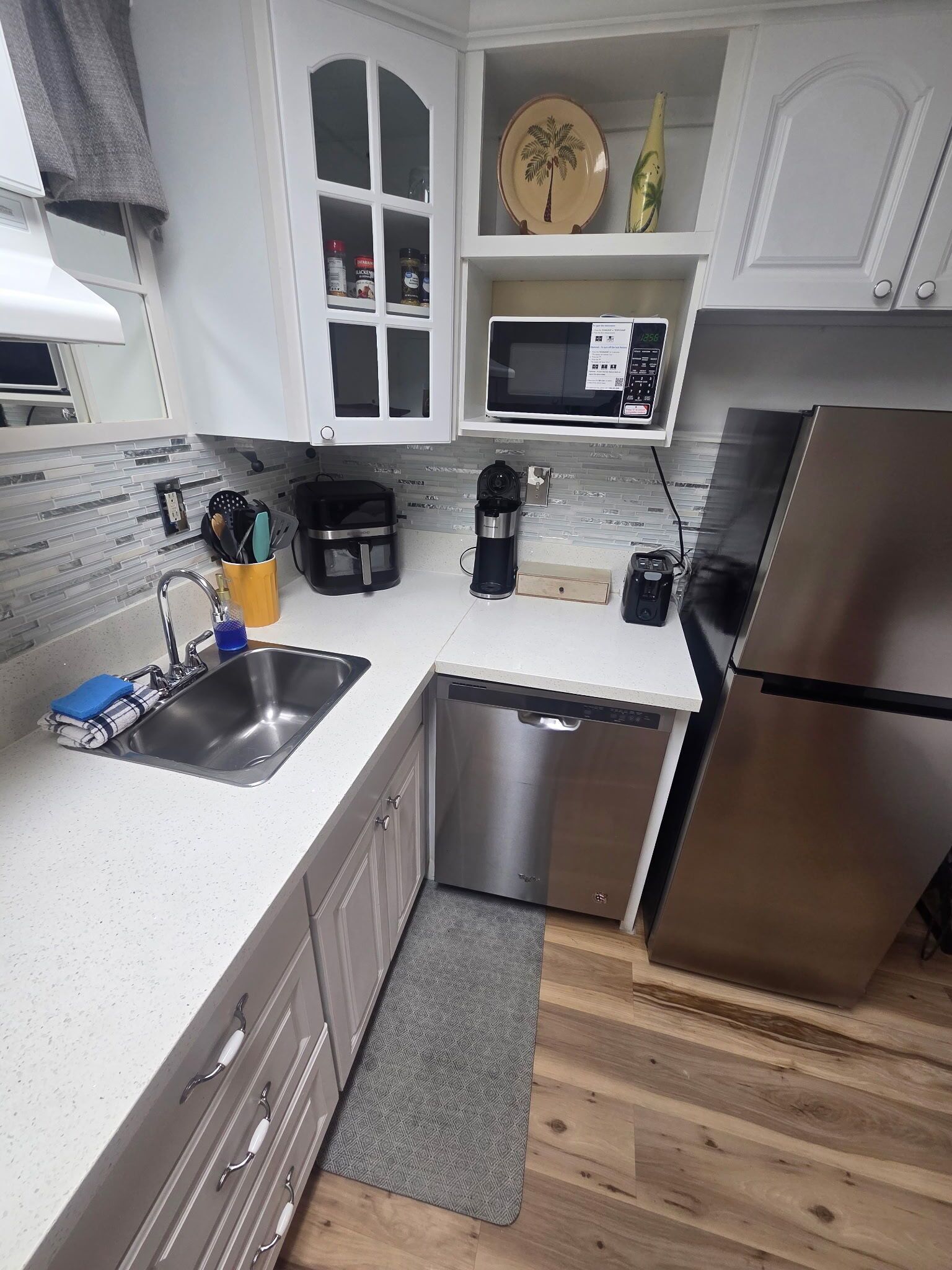 A modern kitchen with white cabinetry, a stainless steel sink, a microwave, a coffee maker, and a refrigerator.