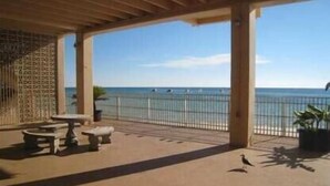 Un espacio al aire libre cubierto con vista a la playa, una mesa y una silla.