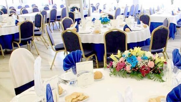 Ein Bankettraum mit runden Tischen, blau bezogenen Stühlen und floralen Tischdekorationen.