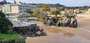A coastal hotel with a stone staircase leading to a wooden deck, overlooking a sandy beach with rocky outcrops. - Hotel Alfar (Arnuero)