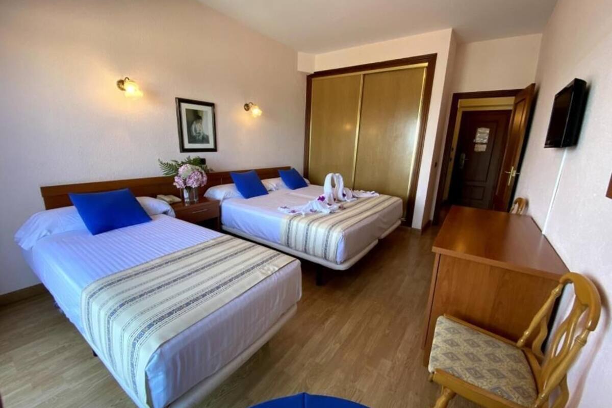 A hotel room with two beds, a wooden desk, a chair, and a wardrobe.