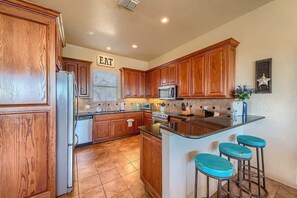 Una cocina con armarios de madera, un refrigerador, un microondas, un lavamanos y una zona de bar con taburetes.
