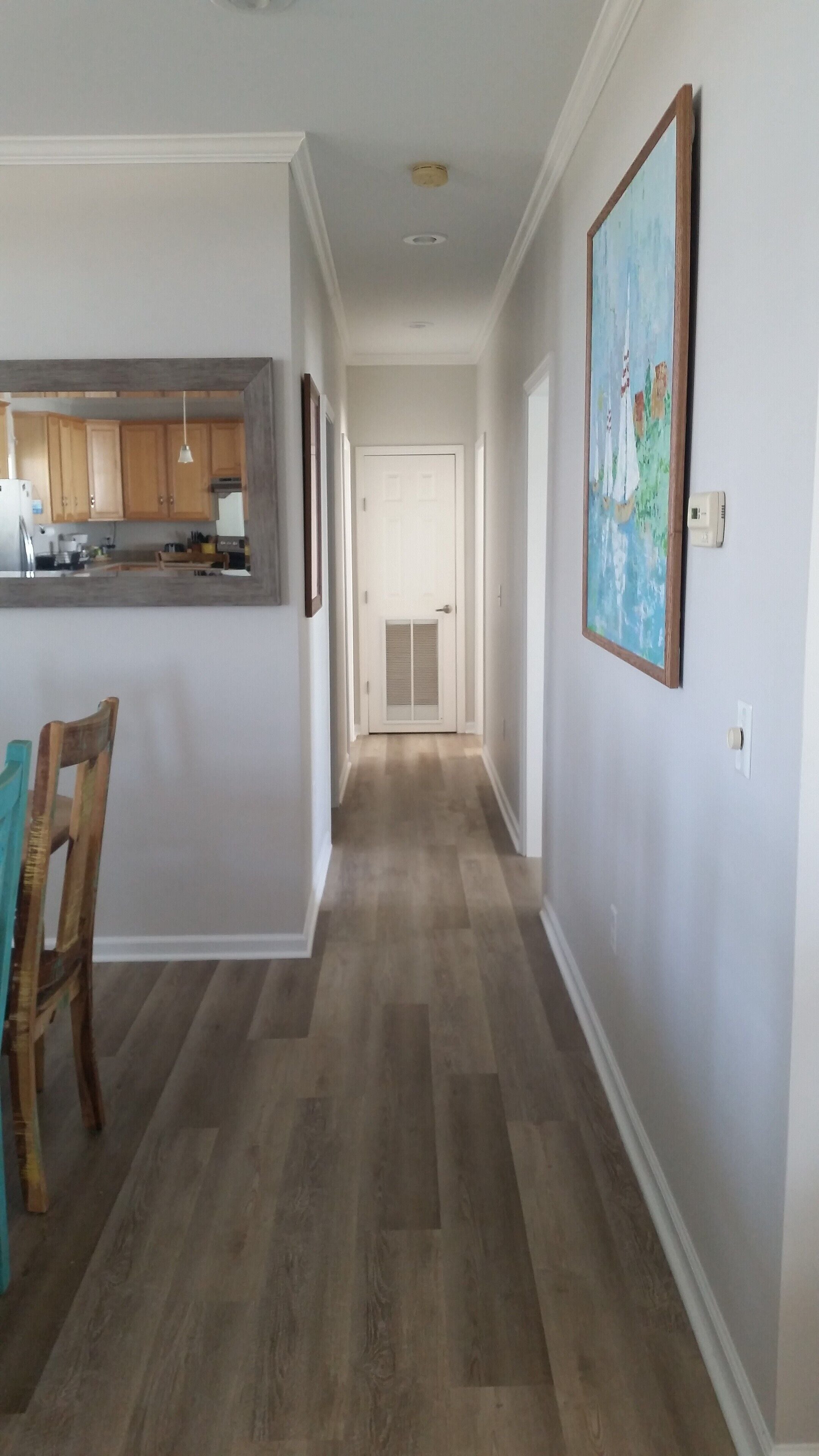 Un couloir avec un plancher en bois, un coin cuisine avec des meubles en bois, et un coin repas avec une chaise et une table.
