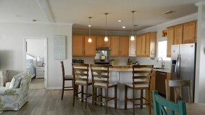 A modern kitchen with wooden cabinets, a central island with bar stools, and a stainless steel refrigerator.