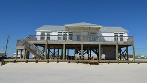 A beachfront house with a wooden deck, multiple balconies, and outdoor seating.
