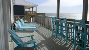 A covered deck with blue chairs and tables, overlooking the ocean.