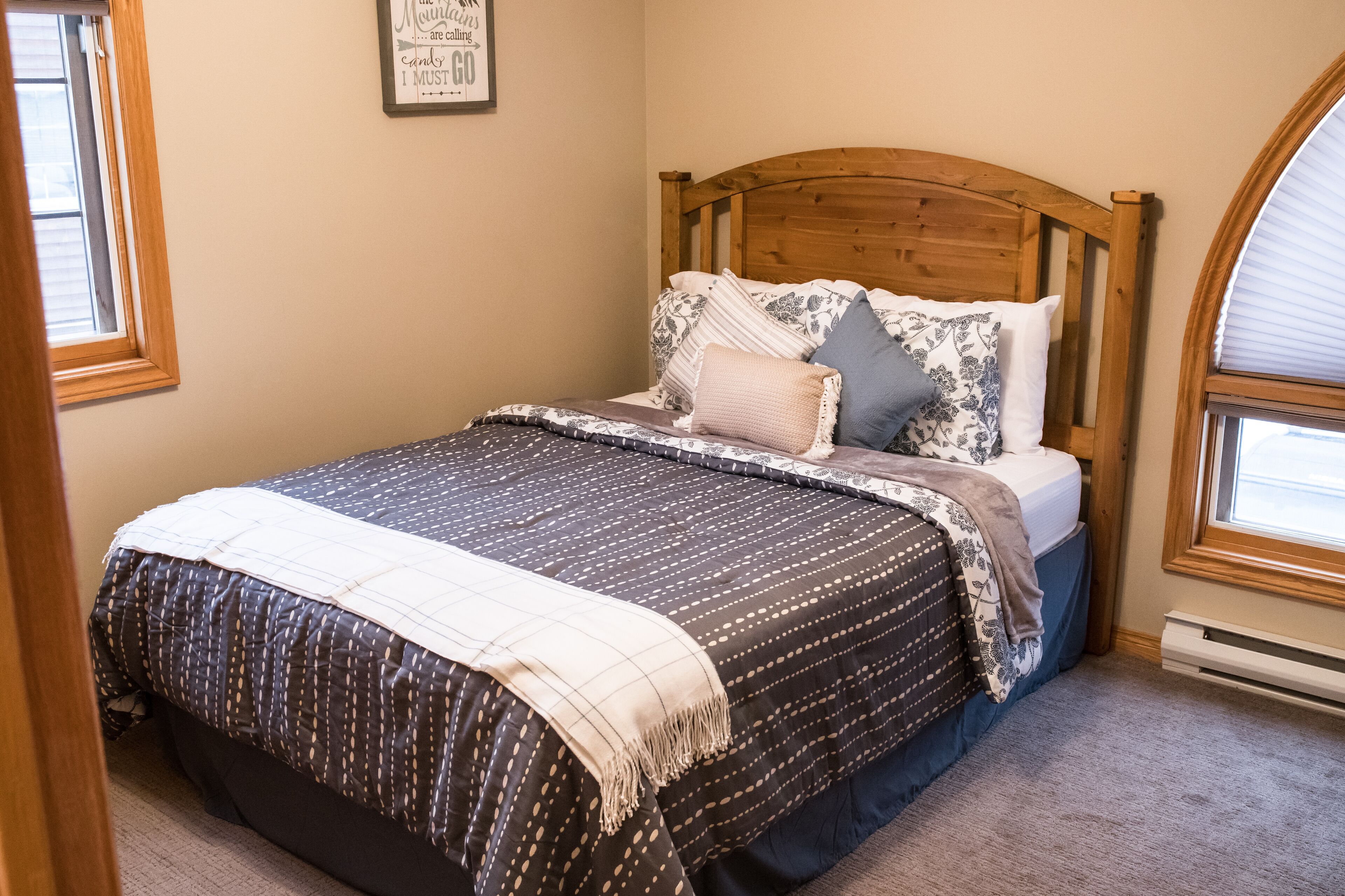 A neatly made bed with a wooden headboard, a patterned bedspread, and multiple pillows.