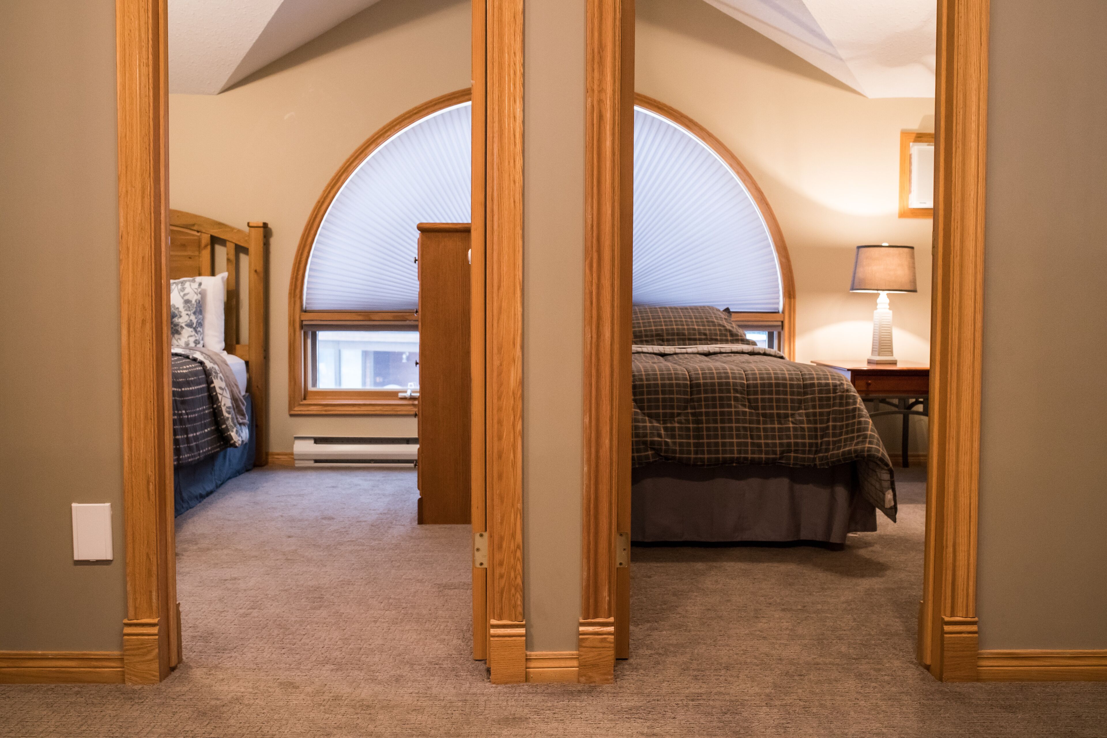 Une chambre à coucher avec une grande fenêtre en arc de cercle, un lit recouvert d’une couverture à carreaux et une table de chevet avec une lampe.